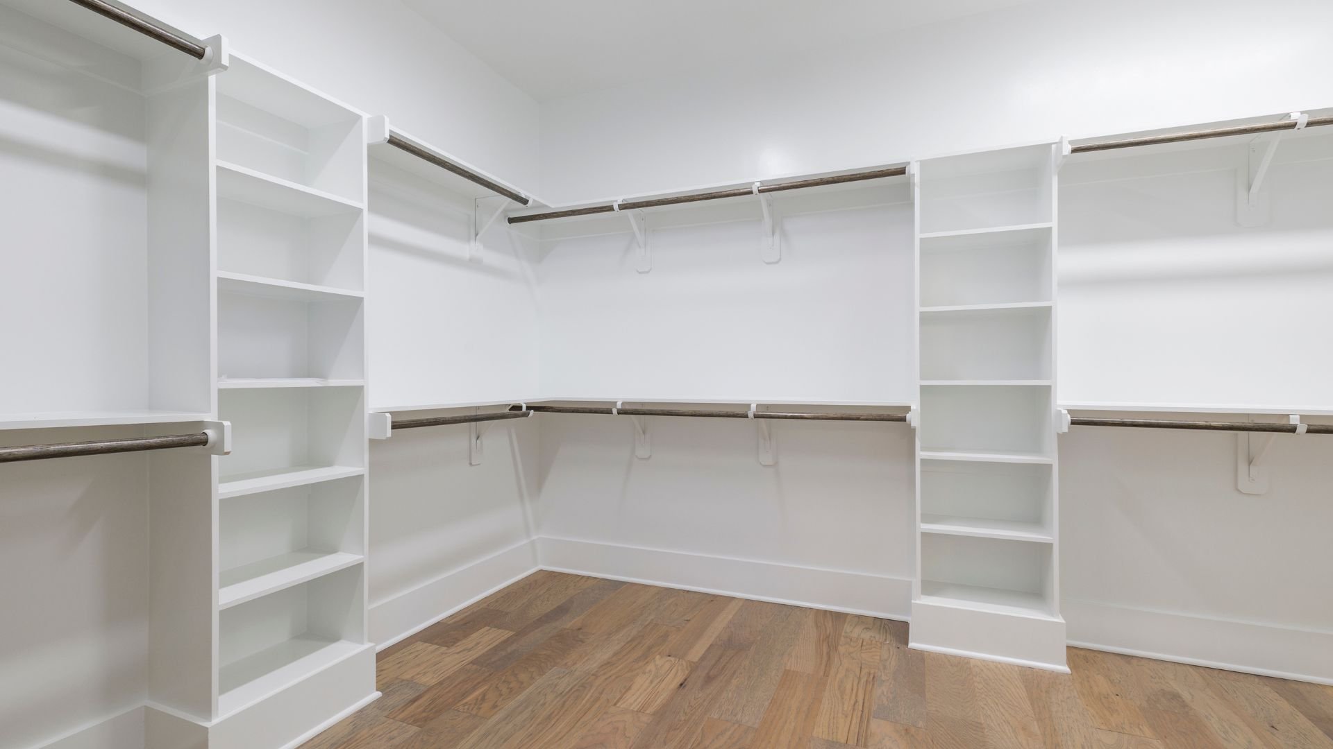 Empty white walk-in closet with wooden floor and multiple shelves