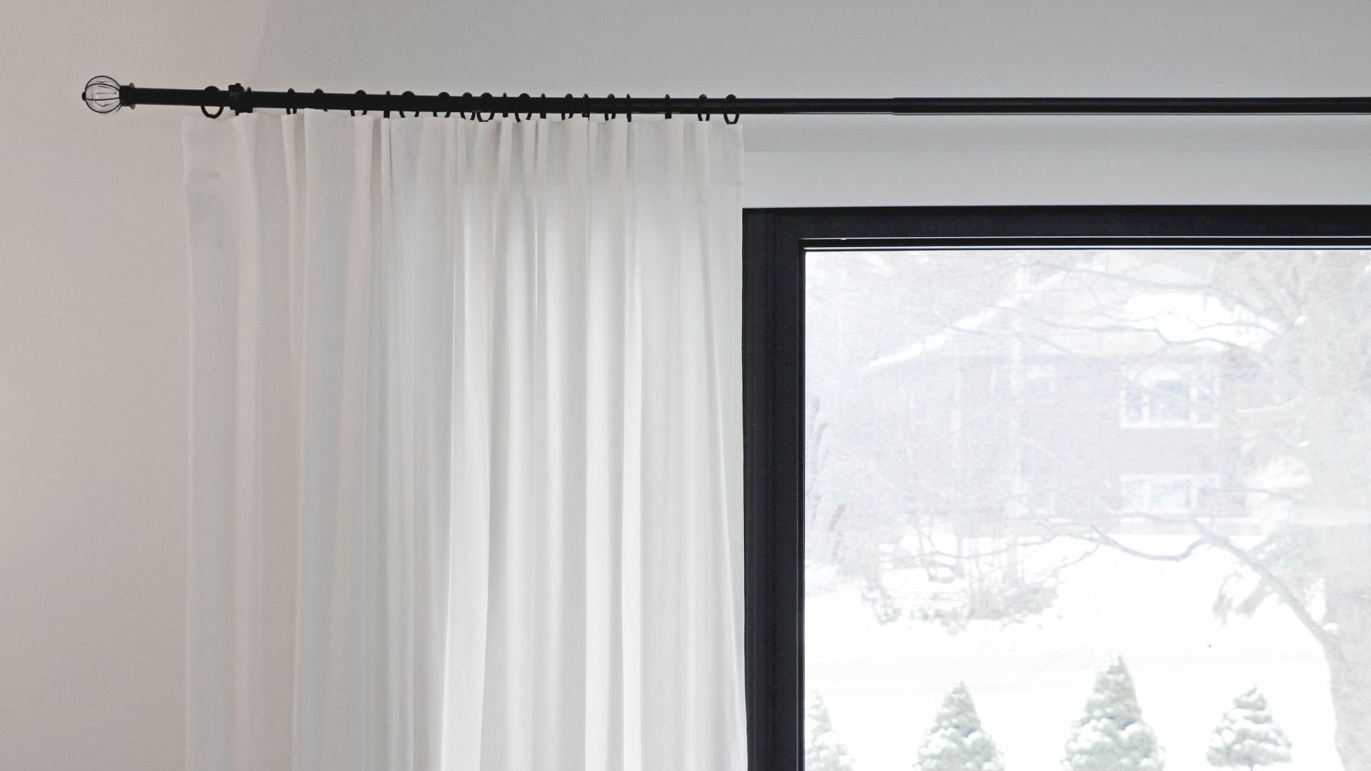 White curtain on black rod with snowy trees visible through window