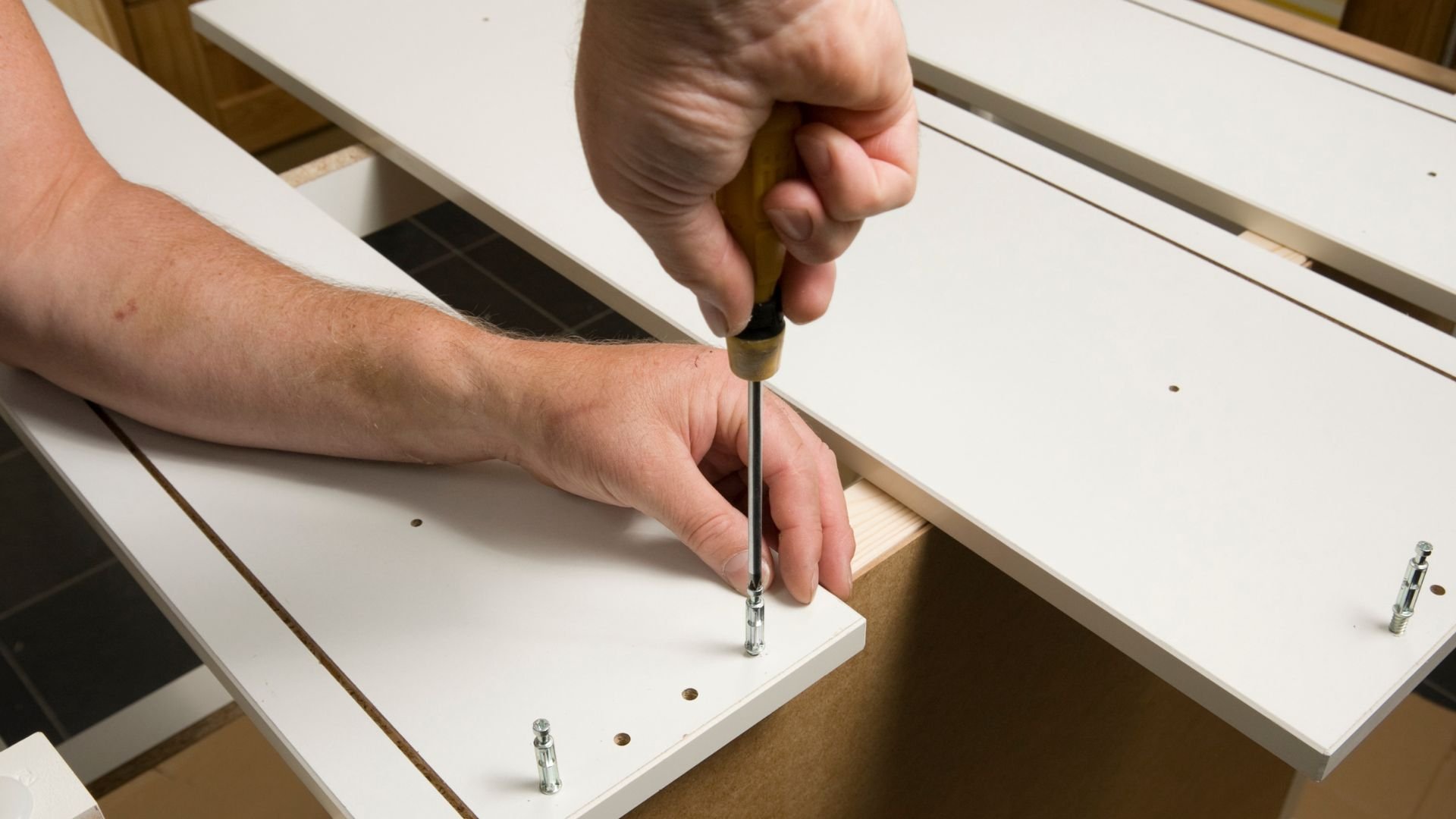 Hand using screwdriver to assemble white furniture or cabinet