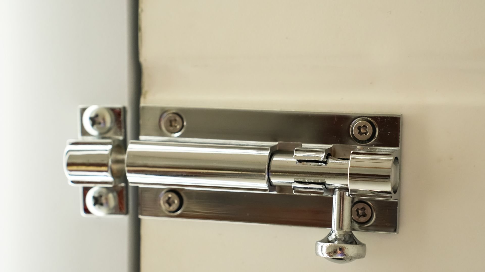 Shiny metal door bolt mounted on a light-colored wall