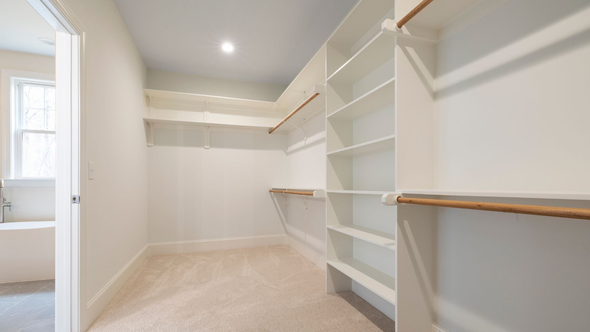 Spacious walk-in closet with white shelves, wooden hanging rods, and carpet