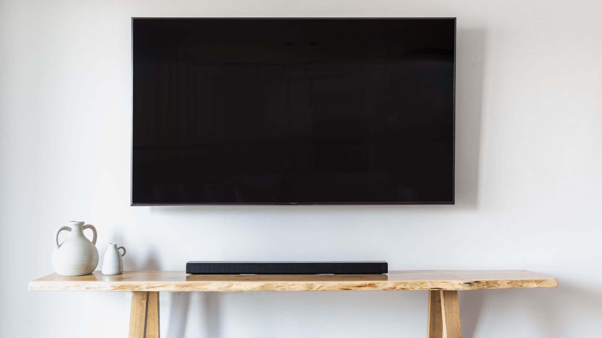 Black flat-screen TV mounted on white wall with soundbar and ceramic vases