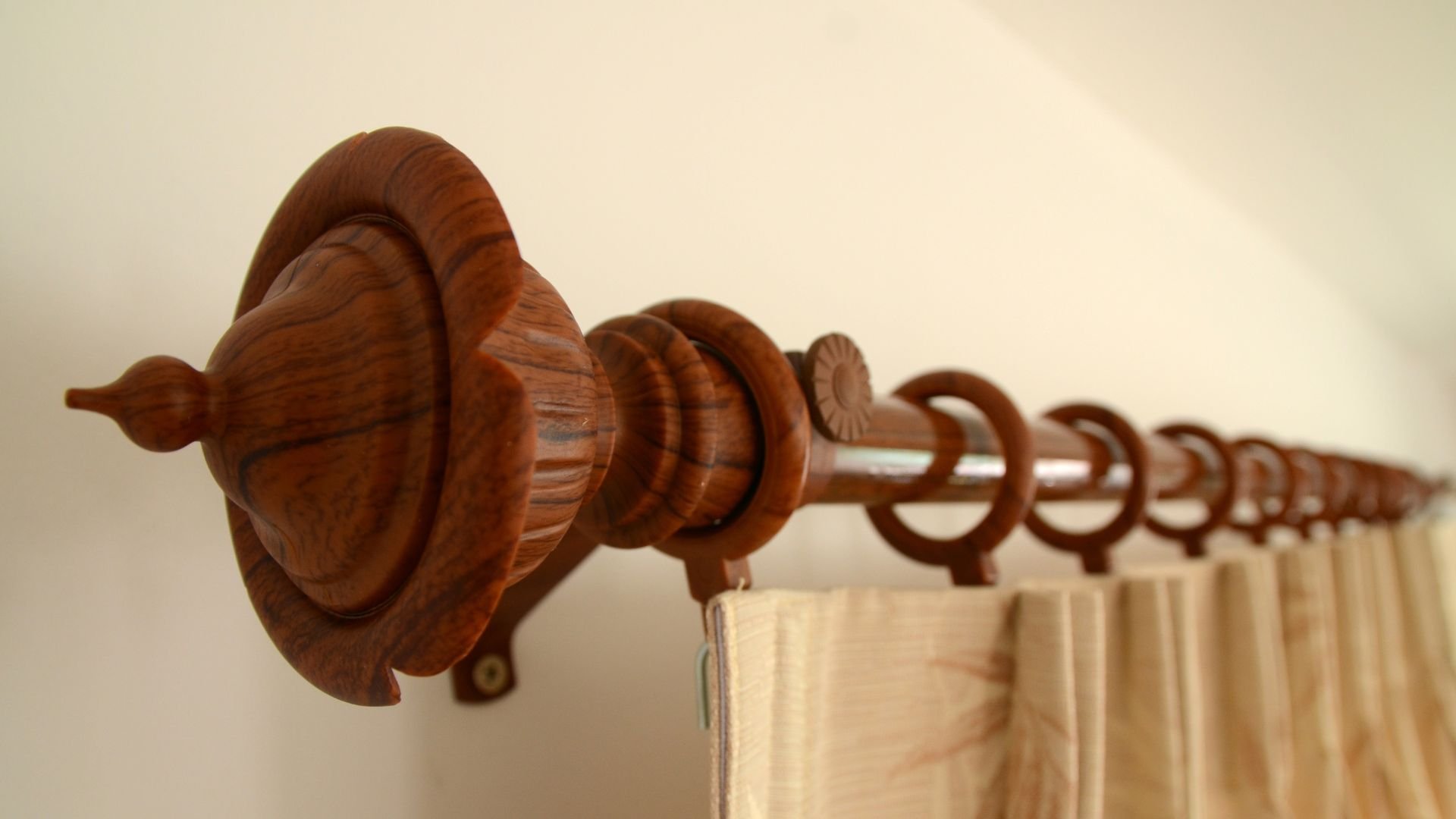Wooden curtain rod with decorative finial and rings, mounted on a light wall